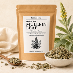 A stand-up kraft paper pouch labeled Farmer Soul Organic Mullein Leaf, shown on a light beige surface with loose dried herb in a wooden spoon and a small bowl, plus soft botanical props in the background.