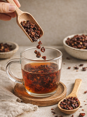 Organic rosehip shells being poured from a wooden spoon into a glass tea mug, showing the loose leaf texture of Farmer Soul botanical tea.